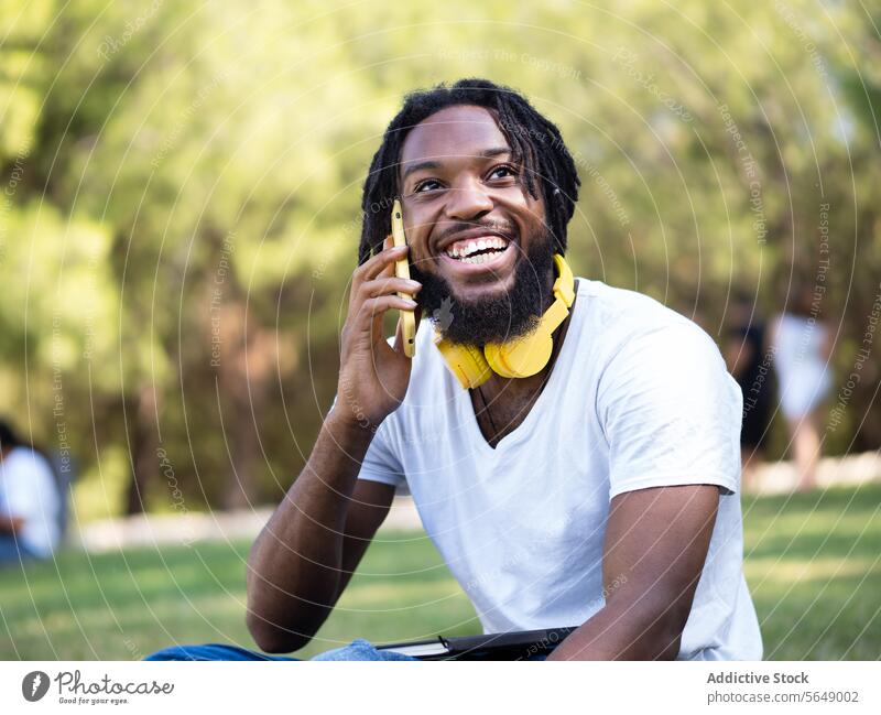 Happy black man having phone call in park hipster headphones using smartphone speak talk summer smile enjoy cheerful male ethnic young african american