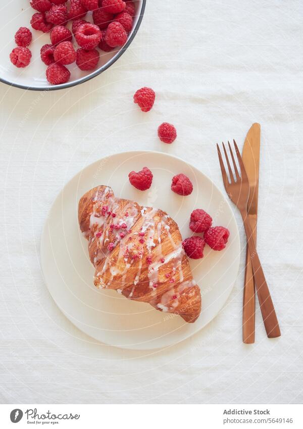 Delicious croissant with raspberry on plate and cutlery placed at marble surface in restaurant delicious food appetizing dish dessert tasty table yummy meal
