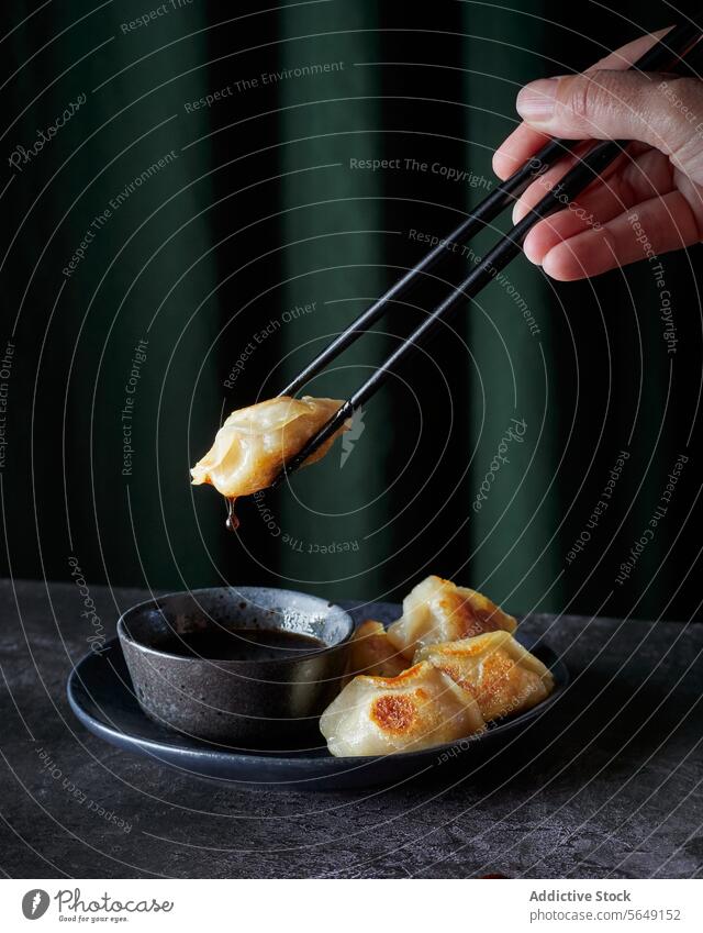 Crop unrecognizable person holding gyoza with chopsticks and sauce in bowl dumpling asian food eat delicious yummy green table tasty dish meal body part