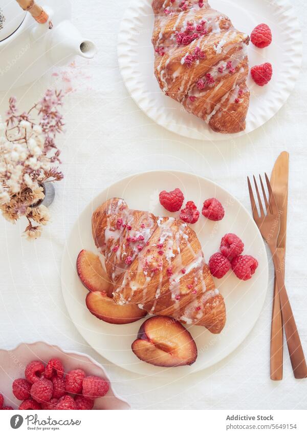 Top view of Croissant and Fruit Breakfast on a White Table near Teapot and cutlery croissant fruit breakfast white tablecloth golden icing colorful sprinkles