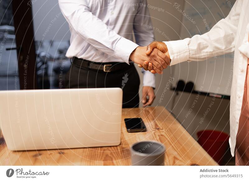 Crop colleagues shaking hands in office near laptop on table smartphone pc project agree handshake coworker greeting deal netbook meeting mobile negotiate