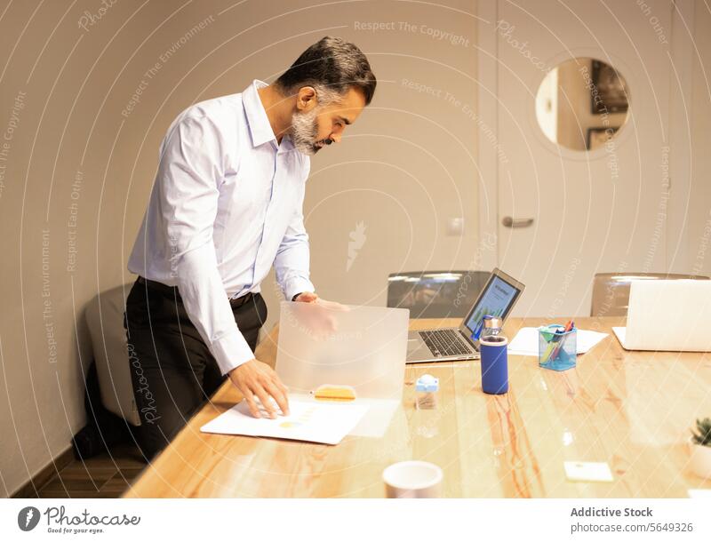 Concentrated businessman checking documents near laptop at table in office professional paperwork netbook entrepreneur concentrate confident suit beard modern