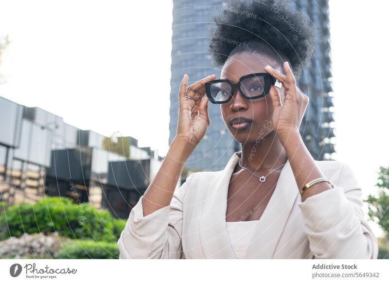 Serious black Businesswoman wearing glasses and blazer looking away while standing against building in city entrepreneur eyeglasses curly hair bun businesswoman
