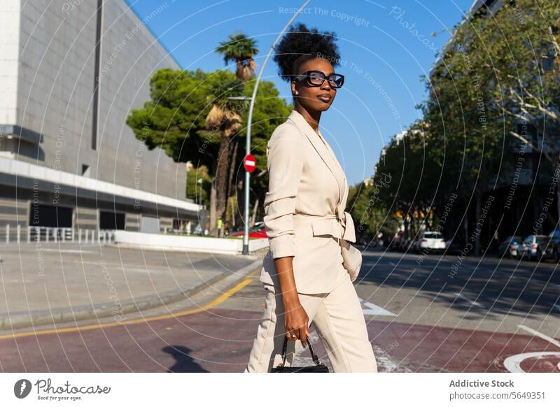Side view of smiling black businesswoman walking on road professional crossing street purse city fashionable sunny sunlight commute stylish urban marking travel