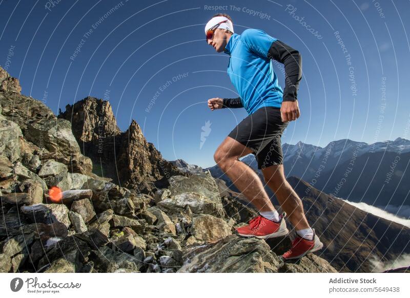 From below of male runner in sportswear ascending rocky alpine path jagged peak mountain trail action focused outdoor running fitness adventure terrain athlete
