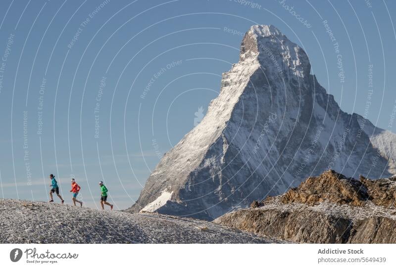 Side view of three athletes in running of trail at Matterhorn sportswear mountain snow background clear sky outdoor fitness alpine adventure exercise travel