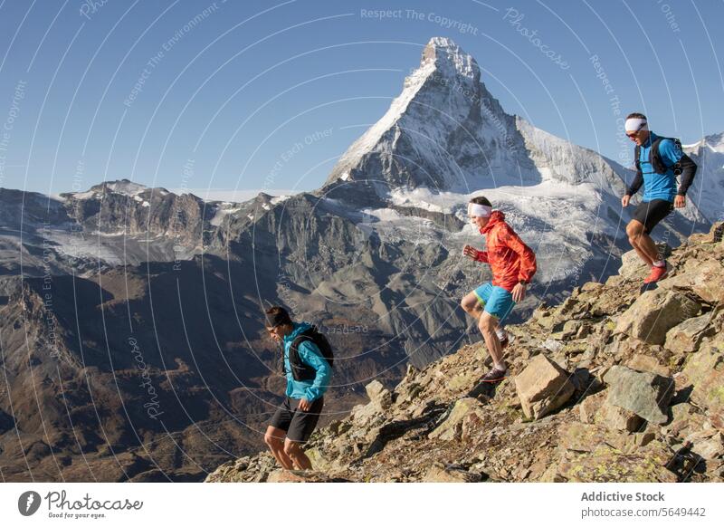 Three people running down a mountain athlete trail rugged path Matterhorn peak clear sky outdoor sport fitness adventure alpine terrain runner exercise travel