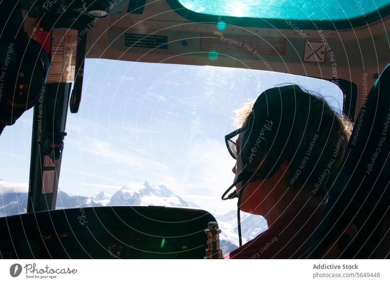 Anonymous of passenger looking out from a helicopter View of Mountain Peak headphones view mountain peak snow blue sky aerial perspective travel high altitude
