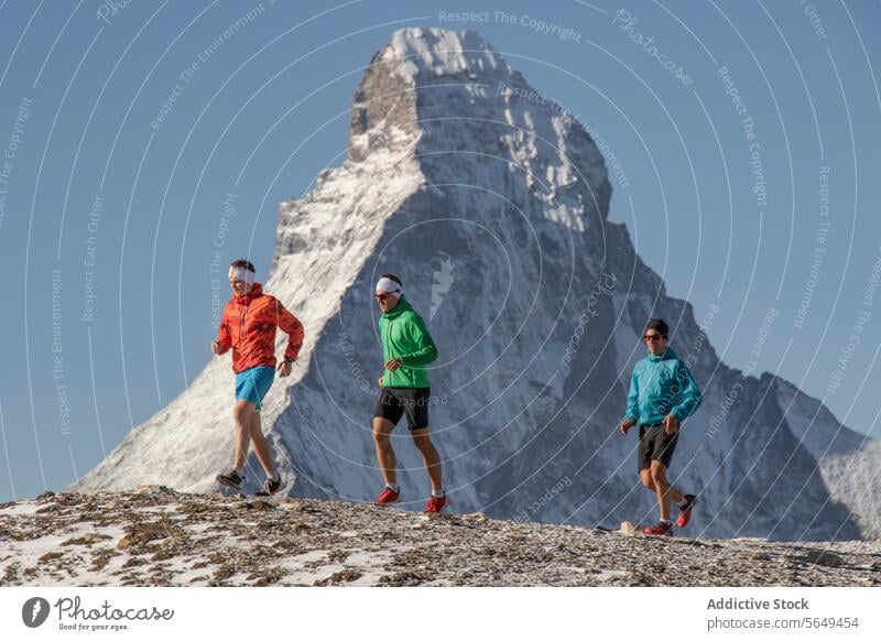 Side view of three athletes in running of trail at Matterhorn sportswear mountain snow background clear sky outdoor fitness alpine adventure exercise travel