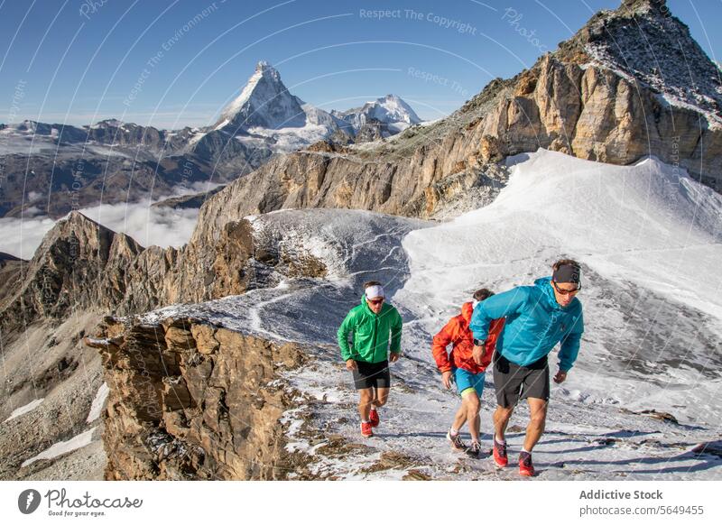 Three trail runners in colorful attire running on a snowy mountain peak path athletic sport endurance exercise fitness nature outdoor adventure trail-running