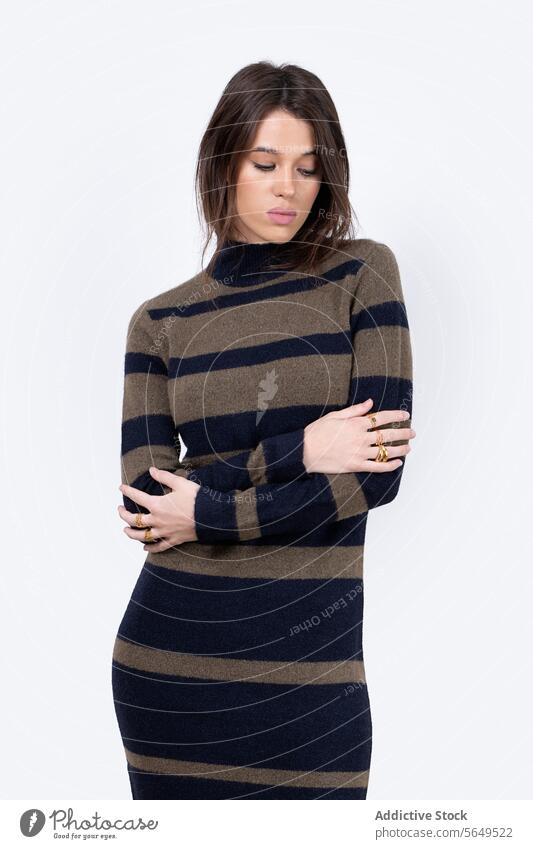 Portrait of confident female model in long sweater dress standing looking down with arms crossed against white background Woman Fashion Model Style Confident