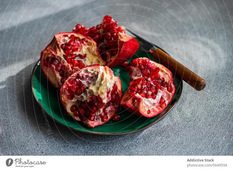 Fresh pomegranate pieces with vibrant red seeds on a green ceramic plate set against a textured grey concrete background fruit juicy ripe open section food