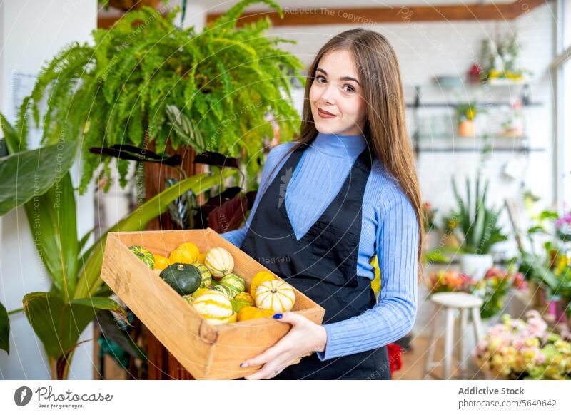 Smiling woman with box of fresh pumpkins in floristry carry work store happy shop owner positive smile female job small business employee young cheerful