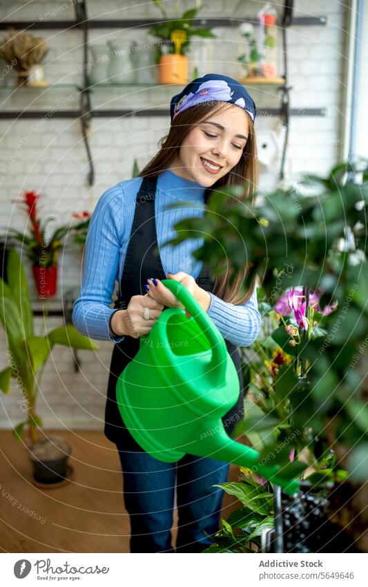 Smiling female florist watering potted plants woman floral shop watering can pour care workday smile young apron small business professional botanic job
