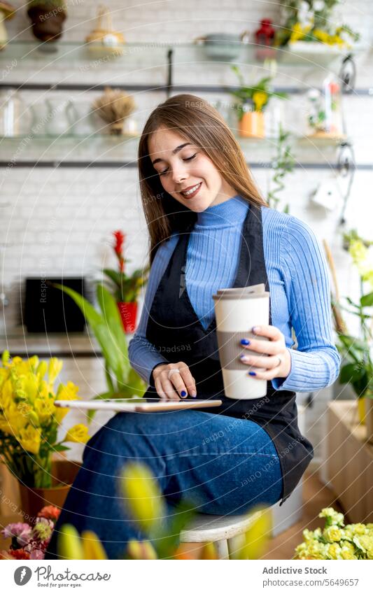 Happy female owner using tablet in flower shop woman florist digital coffee work smile happy young positive device cup workspace floristry store internet online