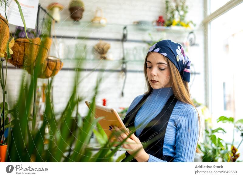 Female florist working in floral shop using tablet woman inventory checklist management potted plant female young apron job profession occupation at work flower