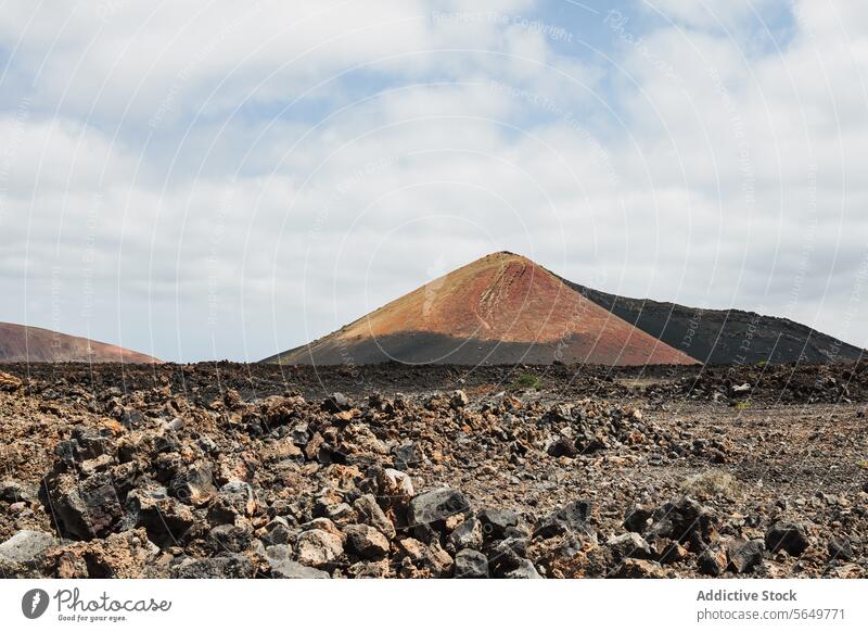 Volcanic cone in Lanzarote in cloudy sky volcanic lava rock landscape rugged nature outdoor scenic barren terrain geology mineral Canary Island panoramic vista