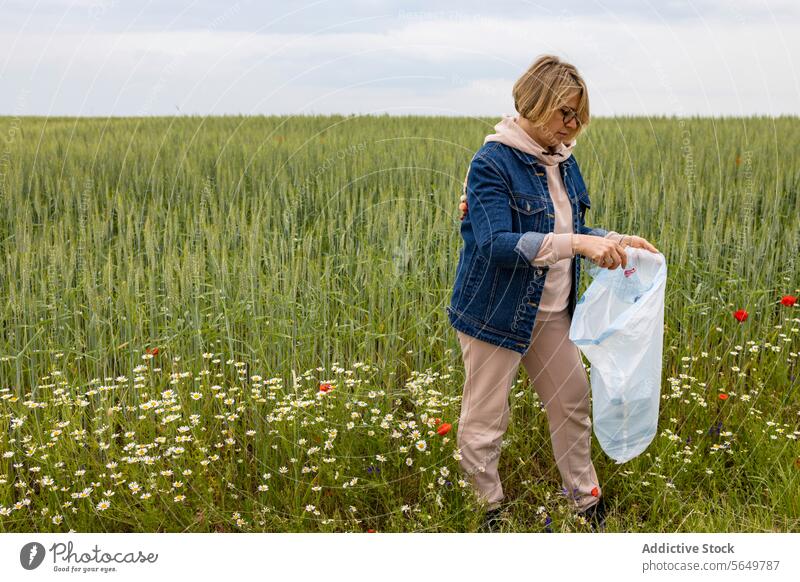 Adult woman standing with a garbage bag collecting plastic waste for recycling meadow wildflowers environment conservation activity eco-friendly education