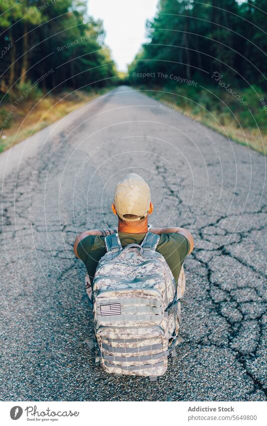 Back view of Anonymous middle aged army commando with backpack sitting on road against forest soldier military anonymous camouflage cap tree unrecognizable