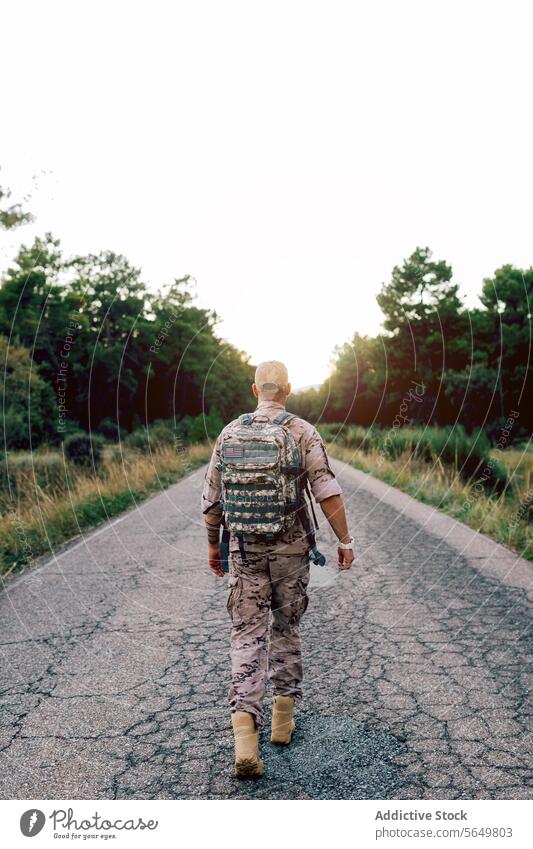 Full body of unrecognizable Mature commando walking on road at sunset soldier camouflage uniform special serviceman military warrior fighter marine patriot