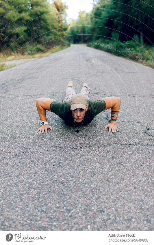 Male military soldier with uniform and cap exercising during training on road against forest man commando pushups fitness exercise routine special force