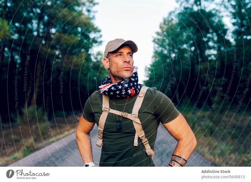 Male commando with American flag wrapped around neck and looking away with pride while standing on road soldier military american confident green uniform blur