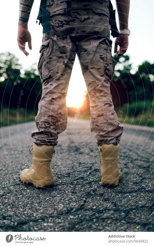 Crop legs of anonymous warrior standing on road during sunset man commando camouflage boot uniform frontline faceless blurred background national special force