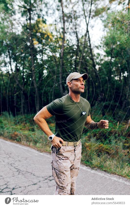 Confident mature male commando running in nature while training in forest soldier military jogging fitness road tree routine confident camouflage green pant cap