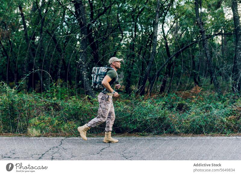 Full body of Soldier training while jogging by plants and trees man commando marine running backpack road fitness uniform soldier roadside camouflage side view