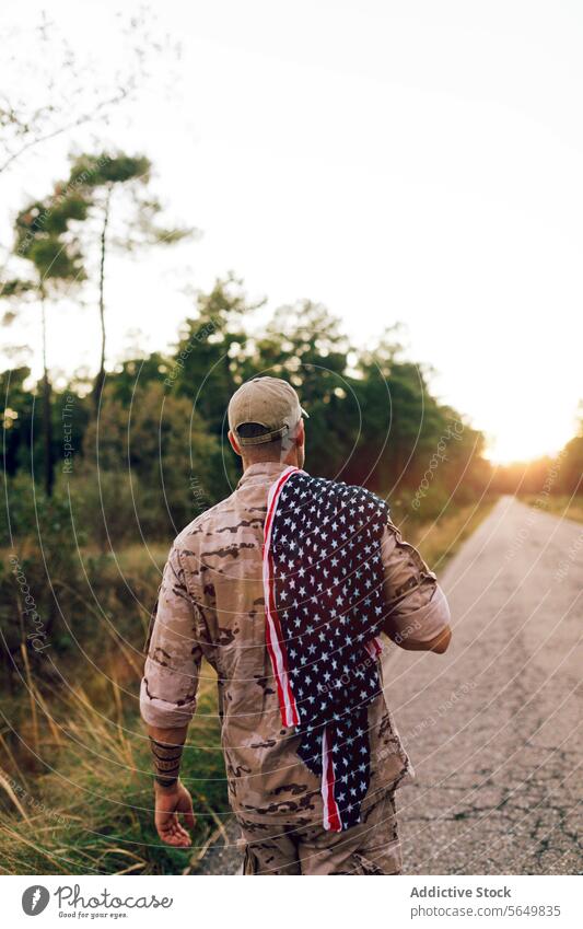 Unrecognizable Mature commando walking on road with American flag on shoulder at sunset soldier american camouflage uniform special serviceman military warrior