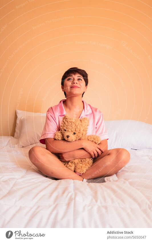 Young woman sitting on bed with teddy bear toy hug smile plush cozy bedroom female young comfort happy pajama sleepwear relax lady peaceful calm cuddle at home