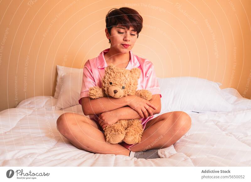 Young woman sitting on bed with teddy bear toy hug plush cozy bedroom female young comfort pajama sleepwear relax lady peaceful calm cuddle at home nightwear