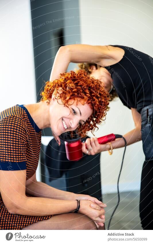 Hairdresser styling a woman's curly hair with a dryer hairdresser red hair hairdryer salon smile modern beauty fashion hairstyle care professional client