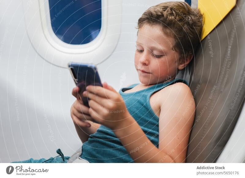Young Boy Engrossed in Tablet on Plane boy child airplane seat tablet cellphone screen technology travel flight window young passenger digital device