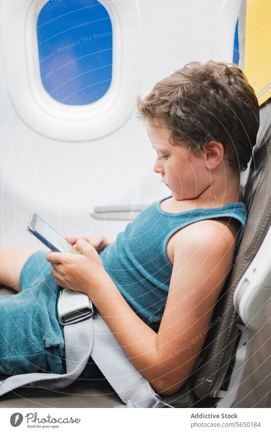 Young Boy Engrossed in Tablet on Plane boy child airplane seat tablet screen technology travel flight window young passenger digital device entertainment