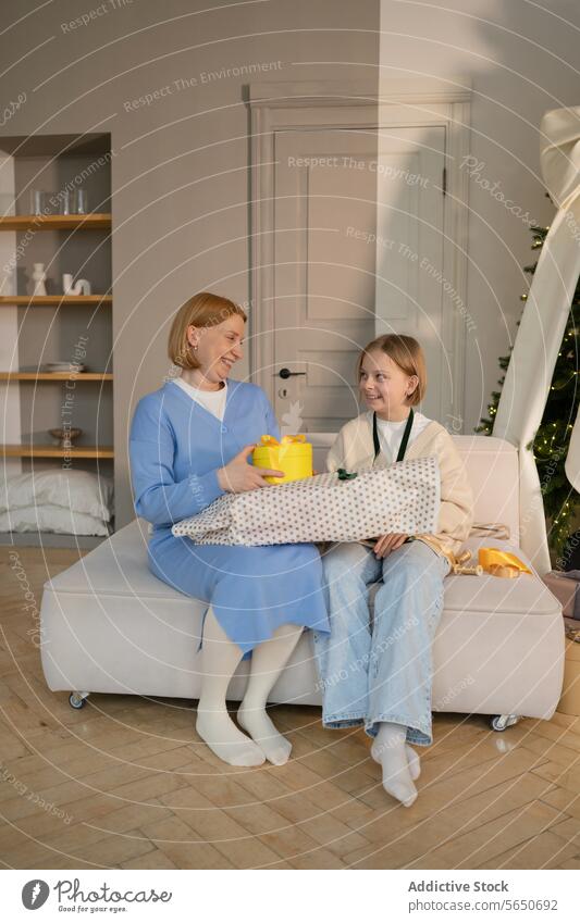 Mother and daughter sharing a joyful gift exchange at home mother sofa smiling present yellow wrapped celebration family happiness bonding indoor festive giving