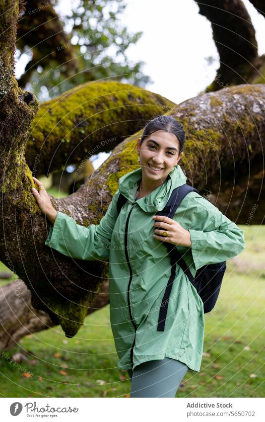 Smiling female hiker in forest with blurred background woman hiking raincoat tree happy moss backpack green standing covering smiling adventure