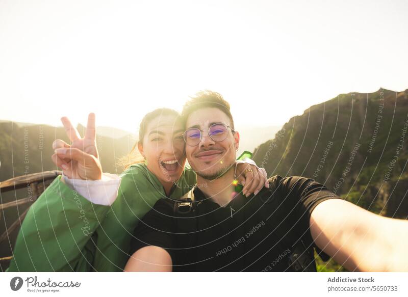 Happy friends at mountain peak during sunrise man woman smiling selfie victory sign backlit portrait cheerful happy together travel signs vacation
