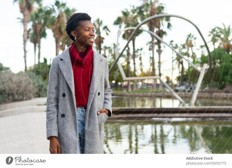 Smiling black woman walking near pond in park city waterfront outerwear weekend autumn free time smile positive happy enjoy stroll cheerful female adult