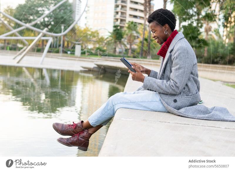 Side view of black woman reading electronic book in park using digital book e book city pond smile positive happy enjoy female adult african american ethnic