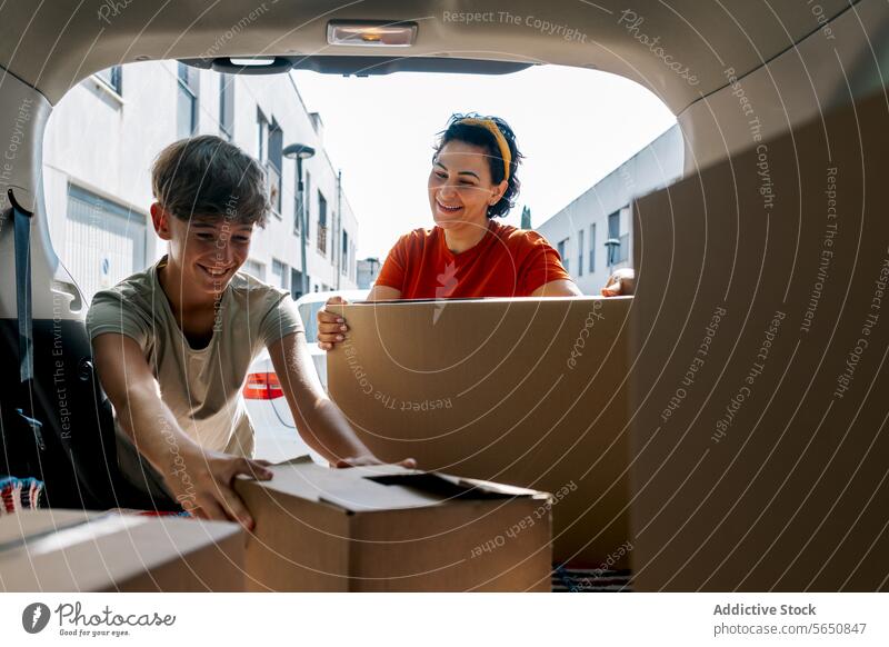 Smiling mother and son picking boxes from car during relocation pick up cardboard move in trunk relocate belonging carton new daytime apartment property unload