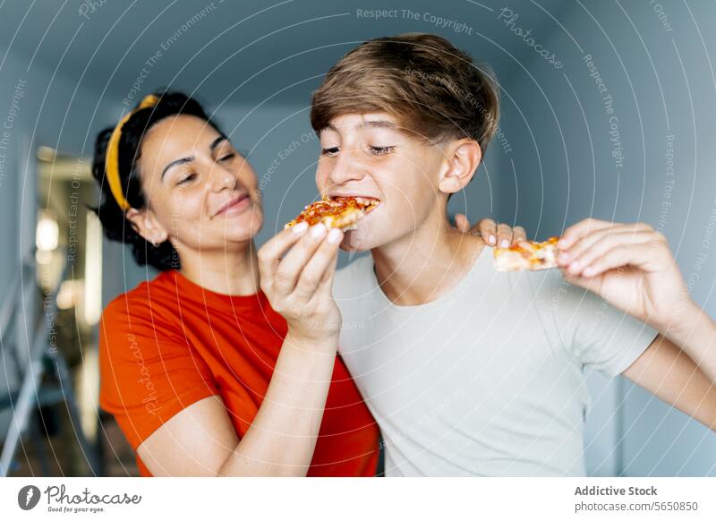 Happy mom feeding son with pizza content mother peace relocate eat home happy together love food smile indoors hungry care boy brown hair positive meal parent
