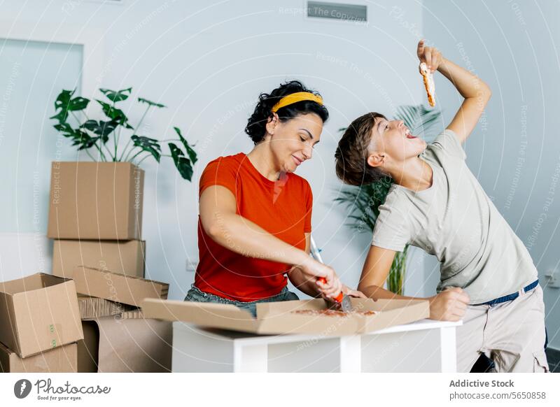 Cheerful mom cutting pizza while son eating piece cheerful relocate cutter happy woman food home lunch mother smile kitchen snack table prepare indoors parent