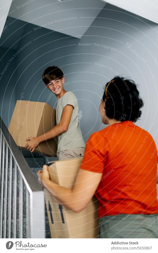Anonymous mother and son carrying boxes in new building move in cardboard together smile apartment relocate home real estate belonging property happy house boy