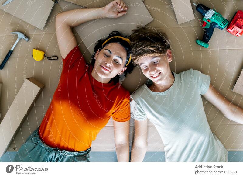 Content mother and son lying on floor surrounded by tools and enjoying moment together during relocation eyes smile relocate new flat home apartment move in