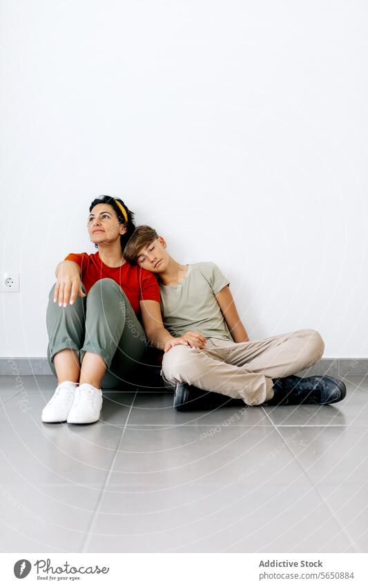Teenager sitting on floor with mother and leaning head on mother shoulder son rest relocate new house teenager parent apartment boy together woman home relax