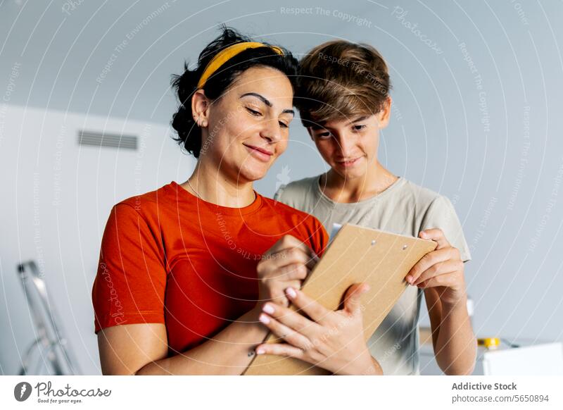 Mother and son checking notes on clipboard together and smiling mother discuss read detail smile woman cheerful happy cooperate teamwork take note conversation