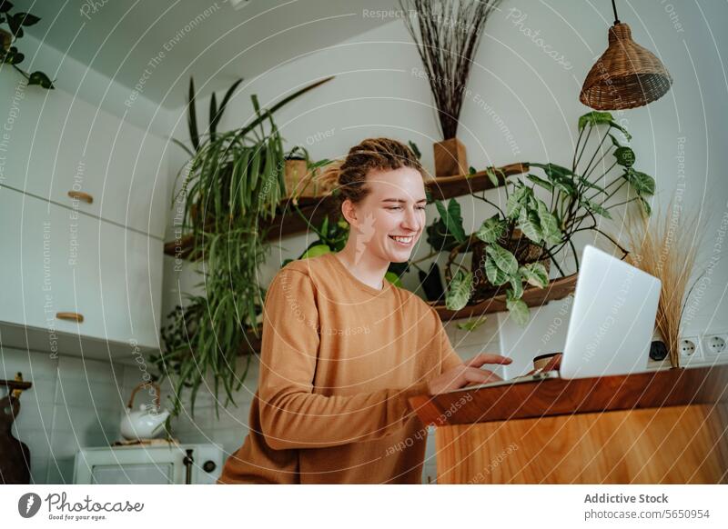Happy Young woman working on laptop at kitchen table with smartphone and coffee mug in daylight cabinet at home female young dreadlocks gadget device mobile