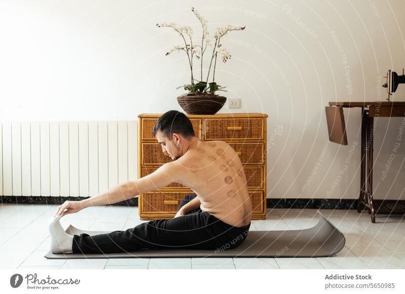 Focused young man sitting on mat and stretching leg during workout at home rehabilitation practice yoga meditate session mindfulness stress relief vitality