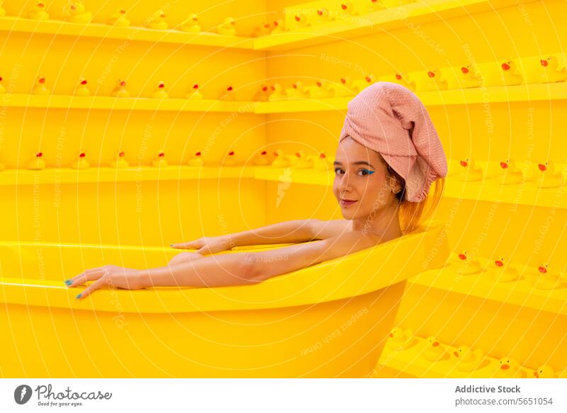 Woman relaxing in the bathtub while looking at the camera woman towel head wrap yellow rubber duck monochromatic leisure self-care beauty calm serene bathroom